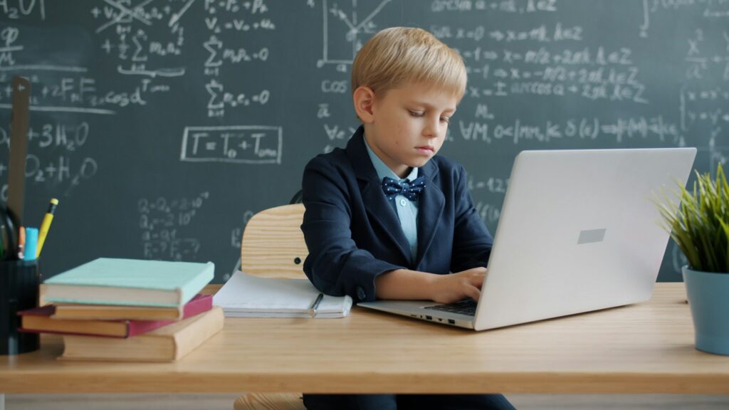 Boy in a suit using a laptop at a desk in a classroom