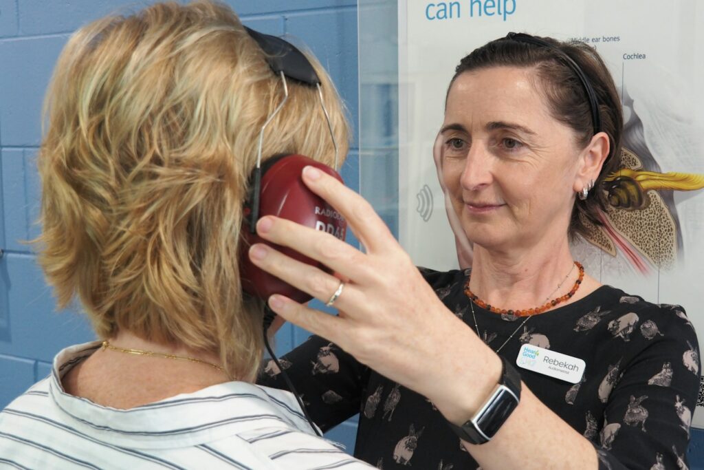 An audiologist placing headphones on a woman before a hearing test